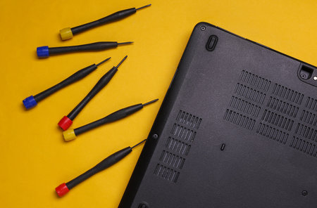 Laptop with screwdrivers on yellow background. Repair of digital equipment and gadgets.