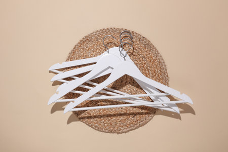 White wooden hangers with straw round mat on beige background. Fashion and style concept. Minimal...
