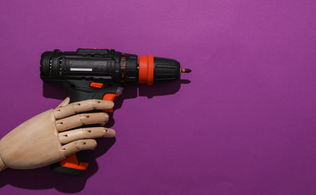 Wooden hand holding cordless screwdriver on purple backgroundの写真素材