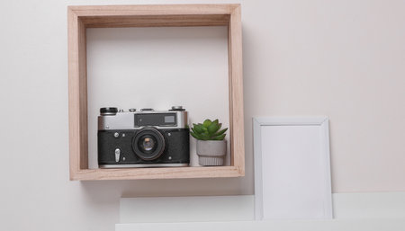 Shelf with white empty photo frame and decor, vases with dry flowers on the wall. Mockup for design