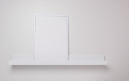 Shelf with white empty photo frame on the wall. Mockup for design