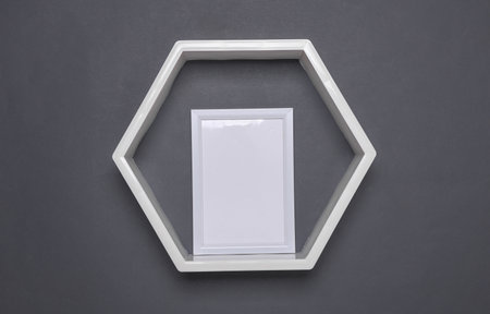 Hexagonal wall shelf with white empty photo frame on dark gray backgroundの写真素材