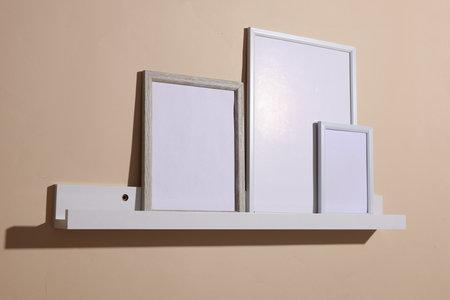Shelf with white empty photo frames on beige background. Mockup for design. Wall decor
