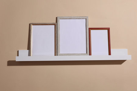 Shelf with white empty photo frames on beige background. Mockup for design. Wall decor