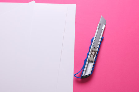 Metal stationery knife and white sheets of paper on a pink backgroundの写真素材