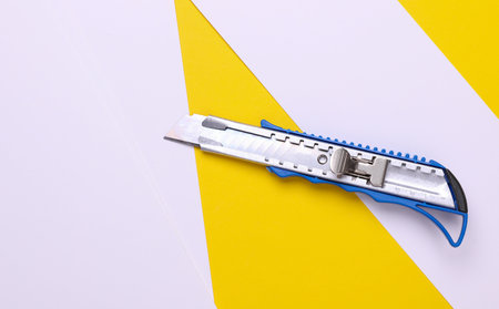 Metal stationery knife on a yellow white background