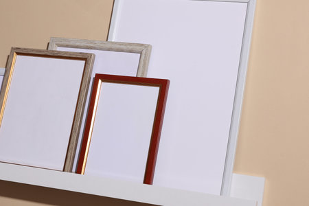 Shelf with white empty photo frames on beige background. Mockup for design. Wall decor
