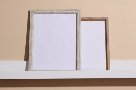 Shelf with white empty photo frames on beige background. Mockup for design. Wall decorの写真素材