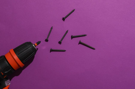 Cordless screwdriver and screws on purple background