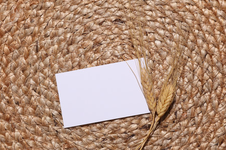 White blank business card with Dried ears of wheat on a woven straw matの写真素材