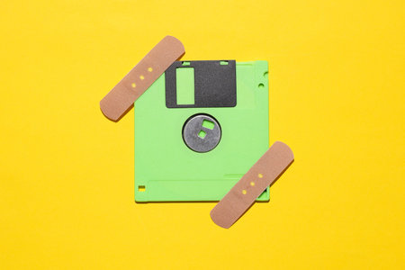Floppy disk with medical plaster on yellow background. Data recovery, repair concept