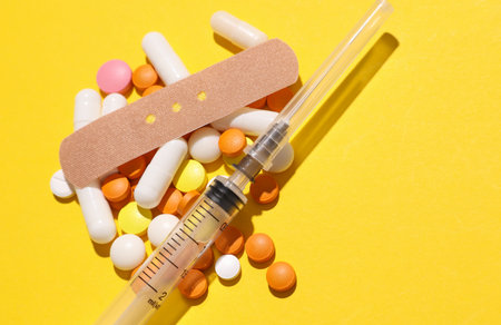 Pills with Medical Adhesive bandage plasters, syringe on yellow background. Top view