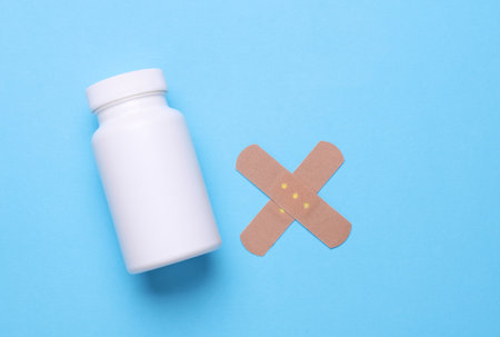 White pills bottle with adhesive bandage plasters on blue background