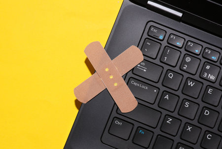 Restoration, repair of digital equipment. Laptop with medical plasters on a yellow backgroundの写真素材