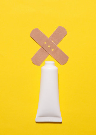 Bottle of cream with medical plaster on yellow backgroundの写真素材