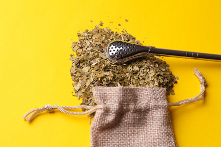 Dry yerba mate in a miniature burlap bag and bombilla on a yellow backgroundの写真素材