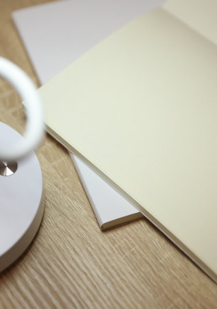 Modern LED lamp illuminates open blank notebook on table. Mockup for designの写真素材