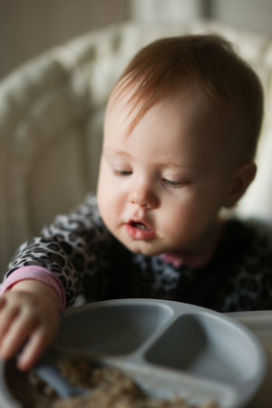 Cute baby eating on his own at the feeding tableの写真素材