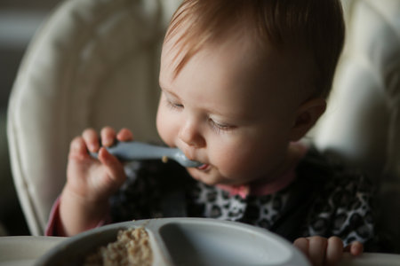 Cute baby eating on his own at the feeding tableの写真素材