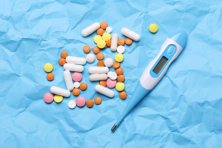 Lots of different pills and thermometer on blue crumpled paperの写真素材