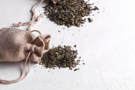 Dry green tea leaves in miniature burlap bags on white concrete backgroundの写真素材