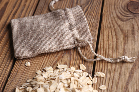 Dry oatmeal in miniature burlap bags on wooden tableの写真素材