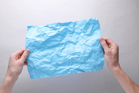 Crumpled blue sheet of paper in hands on gray backgroundの写真素材