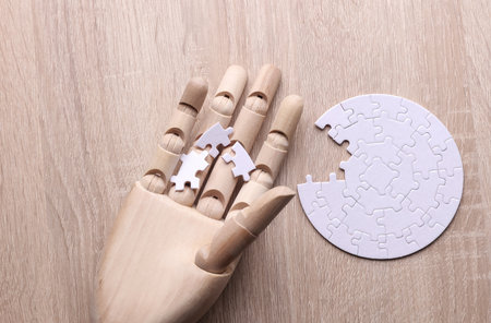 Robotic wooden hand of puppet assembles puzzle on table. Artificial intelligence training conceptの写真素材