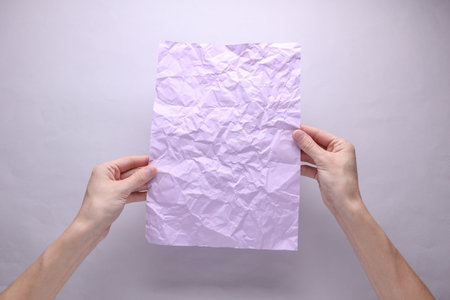 Crumpled purple sheet of paper in hands on gray backgroundの写真素材