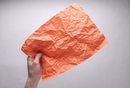 Crumpled orange sheet of paper in hand on gray backgroundの写真素材