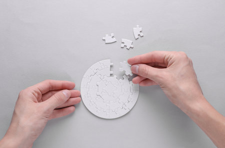 Female hands putting together particles of round white puzzle on gray background. Business concept....