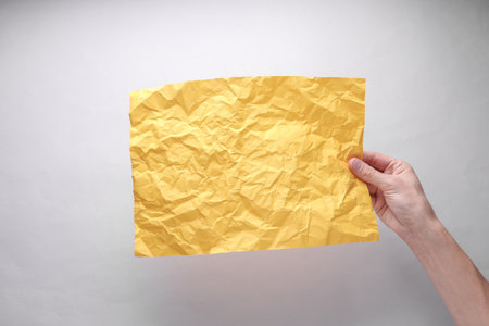 Crumpled yellow sheet of paper in hand on gray backgroundの写真素材