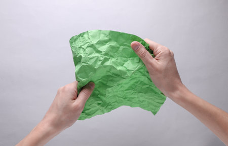 Crumpled green sheet of paper in hands on gray background