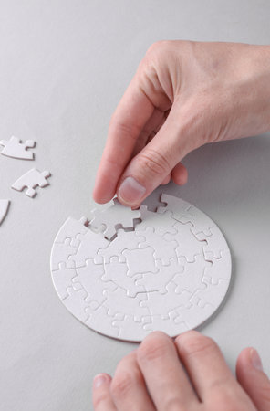 Female hands putting together particles of round white puzzle on gray background. Business concept. Top viewの写真素材