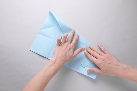 Hands folding blue origami paper on grey background. Top view