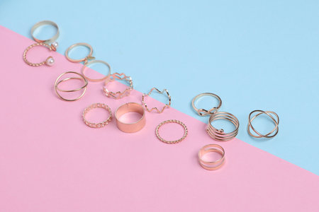 Many Golden rings of different shapes on pink blue background. Jewelry store, beauty concept