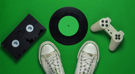Retro old sneakers and vinyl record, gamepad, vhs on green background. 80s. Top viewの写真素材