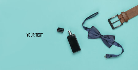Bow tie, belt, perfume bottle on a blue background. Gents accessories, men's business style set. Formal style, preparing for the wedding. Copy spaceの写真素材