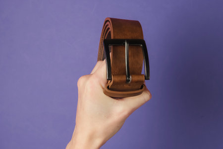Hand holds a leather brown belt on purple backgroundの写真素材