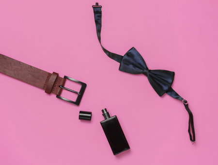 Bow tie, belt, perfume bottle on pink background. Gents accessories, men's business style set. Formal style, preparing for the wedding.の写真素材