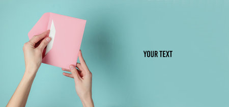 Female hand holds envelope with letter on blue pastel background. Top view. Valentine's day, wedding invitation, letter of loveの写真素材