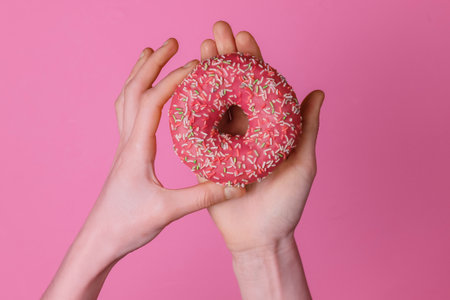 Female hands holding a glazed donut on pink background. Sweet dessert. Top view.の写真素材