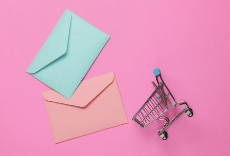 Pink and blue Two envelopes and shopping trolley on pink background. Mockup for valentines day, wedding or birthdayの写真素材