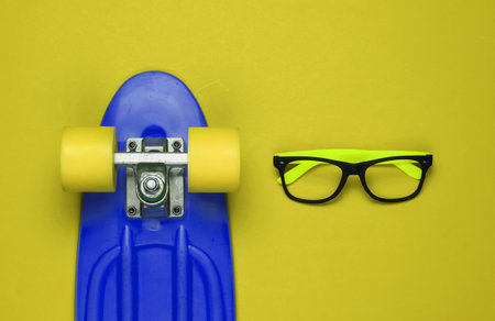 Stylish glasses without lenses, cruiser board on yellow background. Hipster gear. Top viewの写真素材