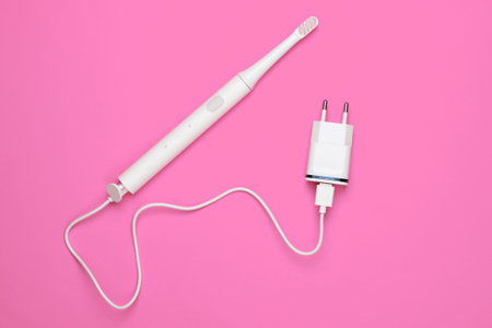 Modern electric toothbrush with a charger on pink background. Top view