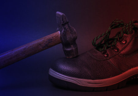 Work leather shoes and hammer in red blue neon light. Strength check, worker safetyの写真素材