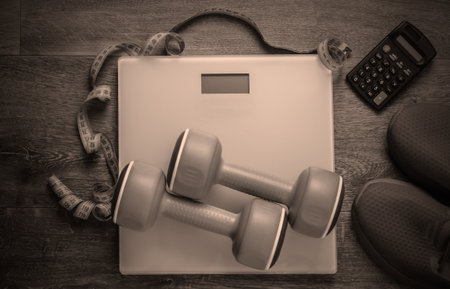 Fitness, slimming, diet concept. Calorie Counting. Floor weights, sneakers, dumbbells, calculator, measuring tape on wooden floor. Top viewの写真素材