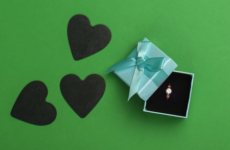 Romantic concept. Golden ring with diamond in box, black hearts on green background. Marriage proposal, gift for Valentine's Day. Top viewの写真素材