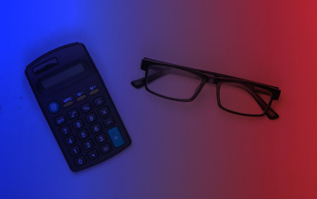 Calculator and classic eyeglasses in neon light. Business concept. Top viewの写真素材