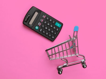 Shopping trolley with calculator on pink background. Economic calculation of shopping, purchase costs. Top viewの写真素材